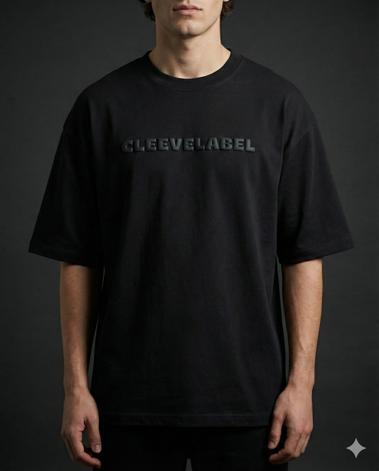 Male model in black oversized Cleevelabel t-shirt with embossed front logo, minimalist studio lighting.