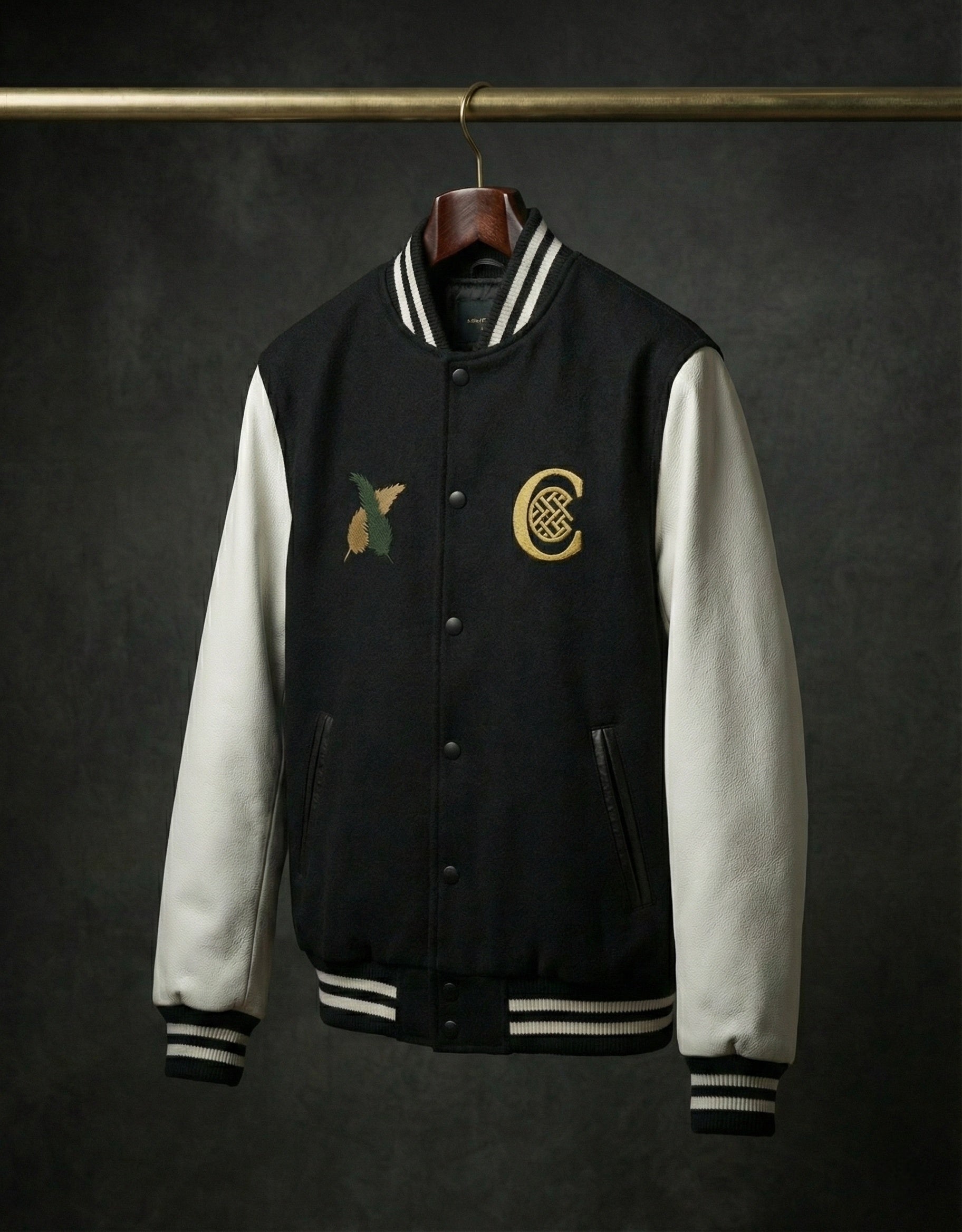 Black and white varsity jacket hanging on wooden hanger with chest patches.