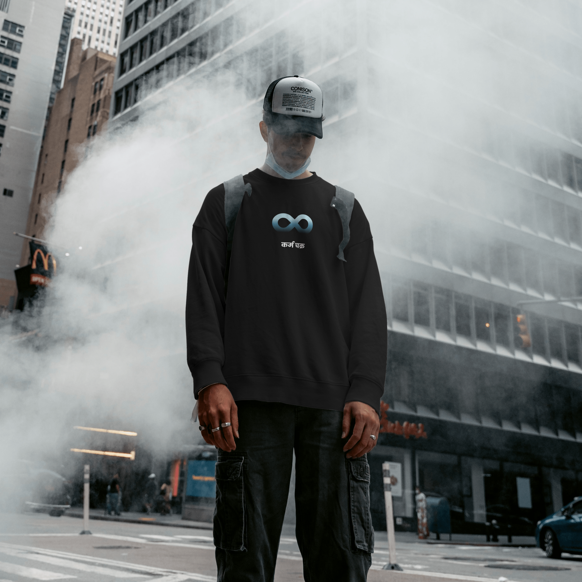 Model wearing black Karma sweatshirt in street setting with infinity symbol on front.